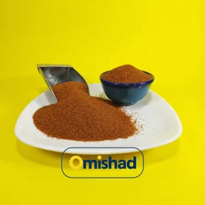 دانه‌های ریز و یکدست خاکشیر اعلا پاک شده بسته 200 گرمی مرغوب با رنگ زرشکی روشن در پیاله آبی سنتی و پیمانه استیل، عکاسی شده در آتلیه اختصاصی میشاد بر روی پس‌زمینه زرد.