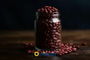 شیشه شفاف پر از لوبیا قرمز خمین دست‌چین عمده 5 کیلویی امیشاد روی میز چوبی با پس‌زمینه تیره و نور طبیعی.