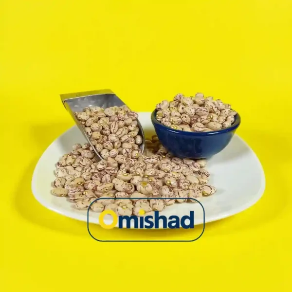 قیمت لوبیا چیتی غزال تیزپای حبوبات 2 لوبیا چیتی خمین داخل کاسه و سر تاس فلزی روی بشقاب سفید با پسزمینه زرد.
