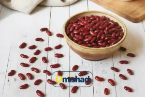 کاسه سفالی پر ازلوبیا قرمز خمین دستچین بسته 900 گرمی روی میز چوبی سفید با دانه‌های پخش‌شده و لوگوی امیشاد.