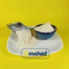 پودر پیاز اعلا در ظرف آبی و بیلچه فلزی روی بشقاب سفید.