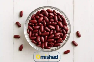 کاسه شیشه‌ای پر از لوبیا قرمز خمین دست چین عمده 30 کیلویی روی میز چوبی سفید با چند دانه پراکنده و نور طبیعی نرم.