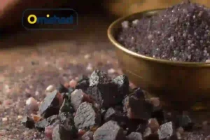تکه‌های طبیعی نمک سیاه هندی کالا نمک در کنار کاسه فلزی پر از دانه‌های تیره نمک امیشاد.