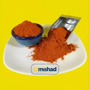 پودر فلفل قرمز نرم اعلا خارجی یک کیلویی در کاسه آبی و بیلچه فلزی روی بشقاب سفید با پسزمینه زرد.